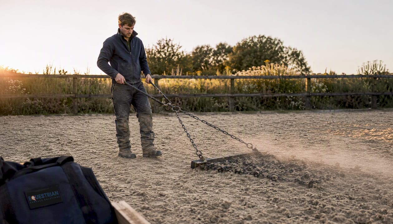 Groom harrowing fibre sand footing in arena